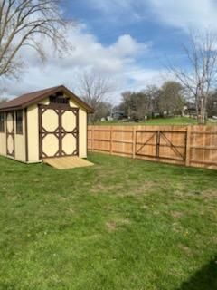 Backyard with tan shed, wooden fence, green lawn, and partly cloudy sky