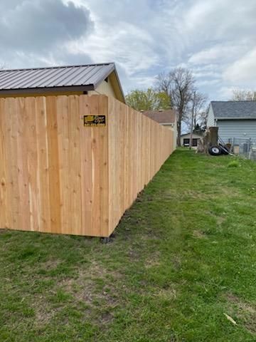 Wooden fenced enclosure beside a grassy yard, with a metal-roofed shed and cloudy sky in the background