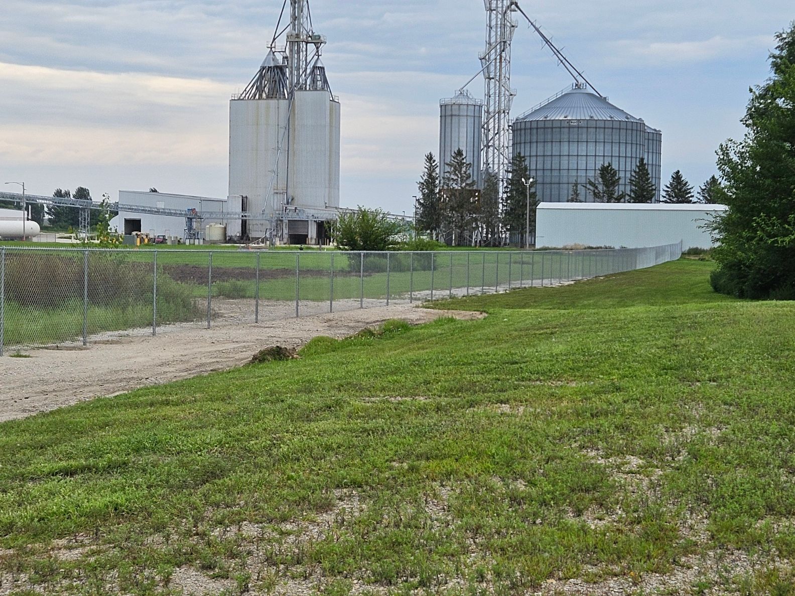 Industrial grain silos beside a green field under a cloudy sky