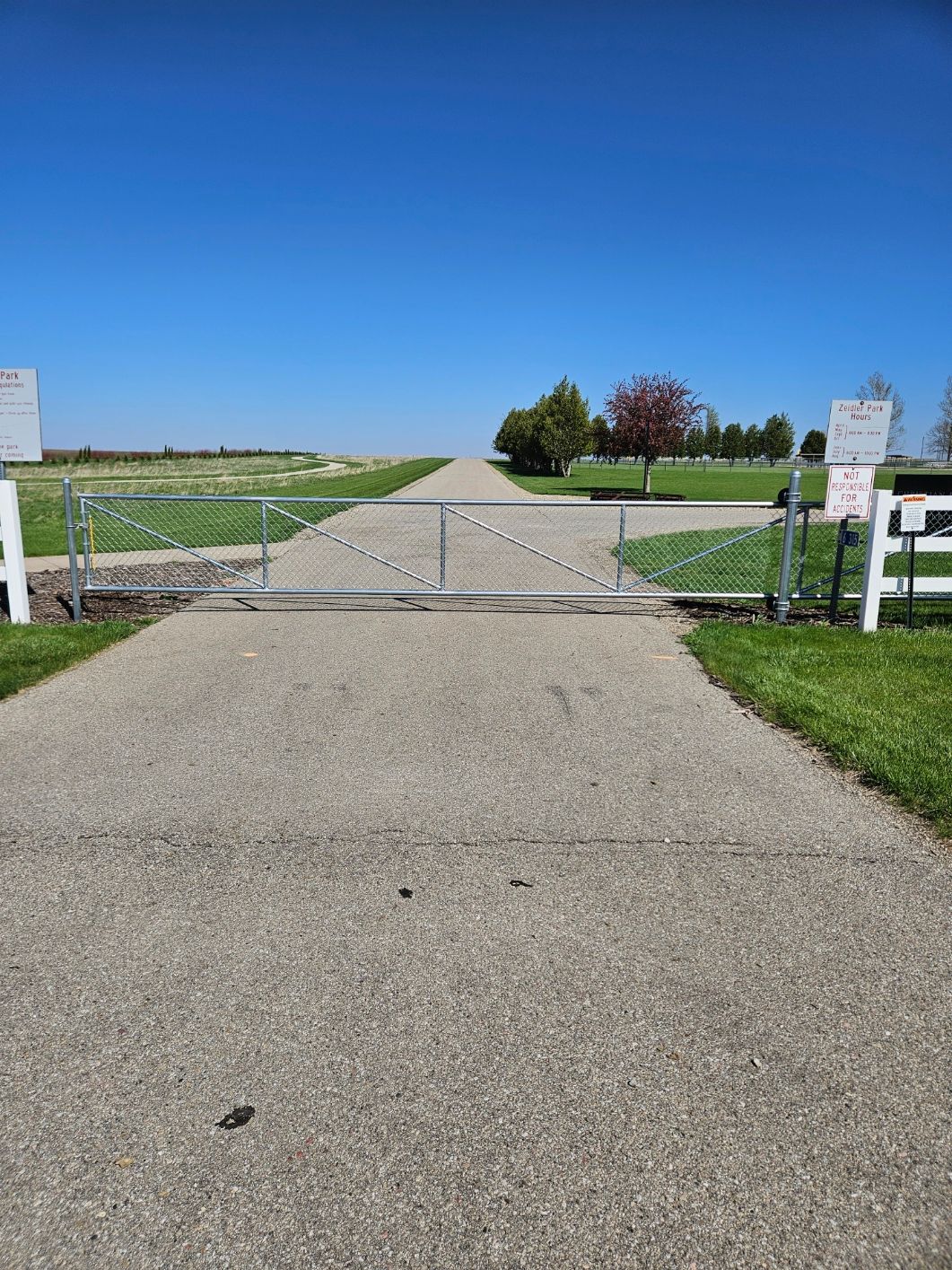 Gravel path leading to a closed gate and open grassy fields under a clear blue sky