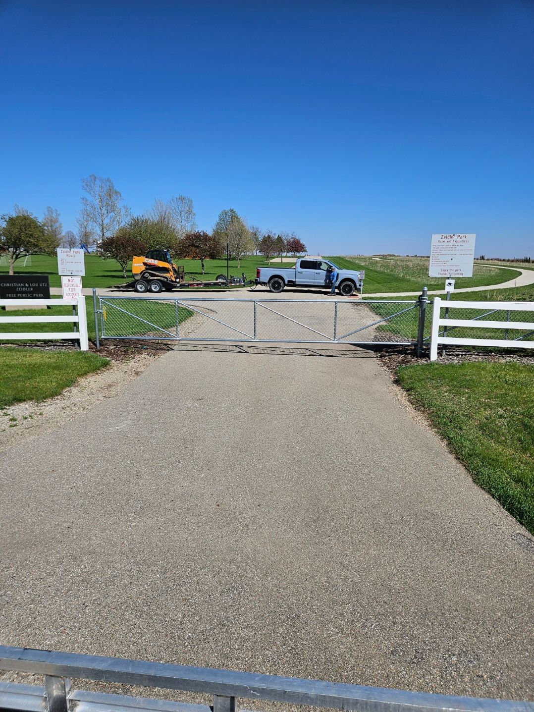 Gravel driveway with white gate, parked truck, and open countryside under a clear blue sky