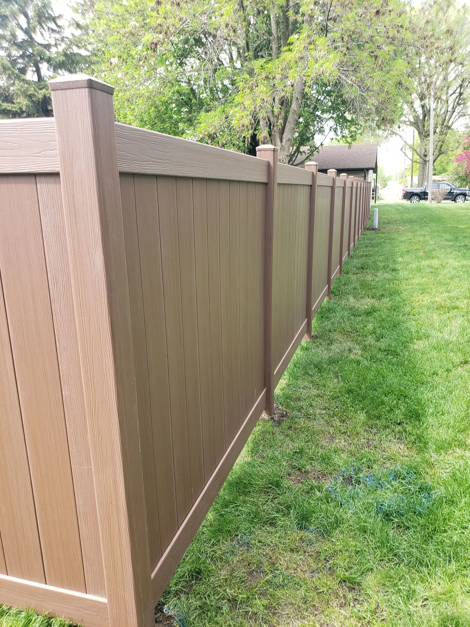 Brown wooden privacy fence along a grassy yard with trees in the background