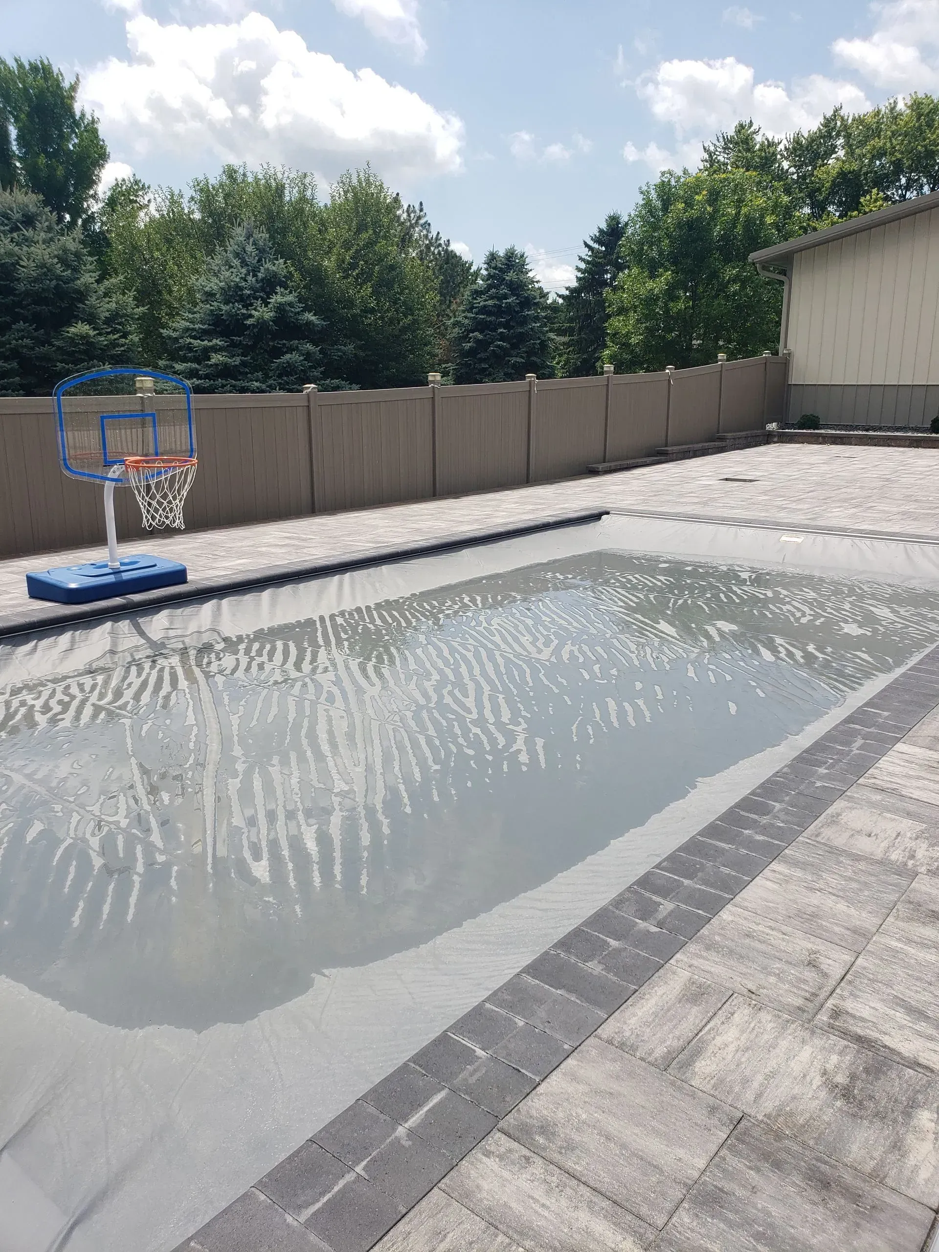 Backyard pool being refilled, with a portable basketball hoop beside the empty waterline.
