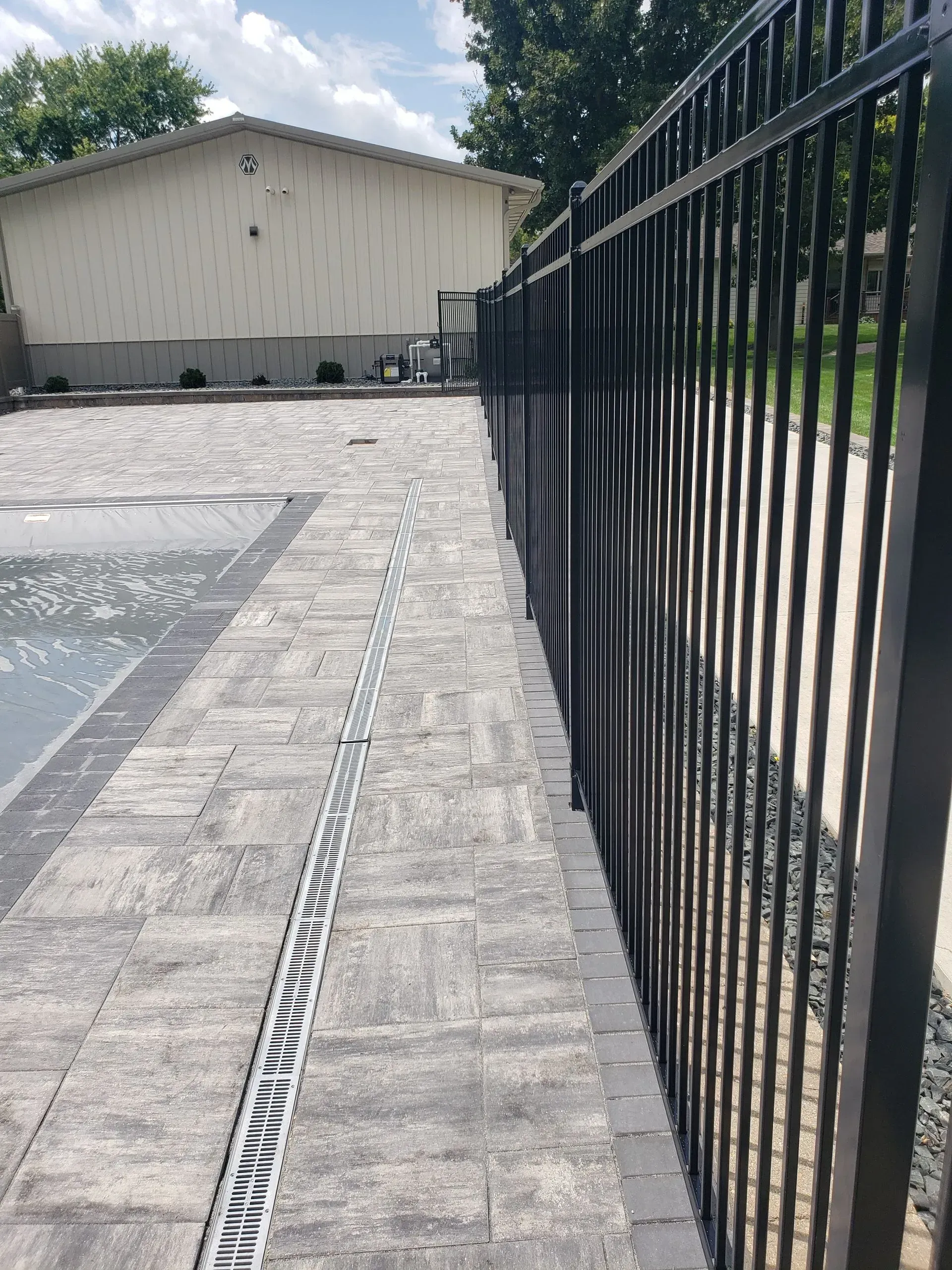 Paved walkway beside a black metal fence leading to a beige building under a bright sky