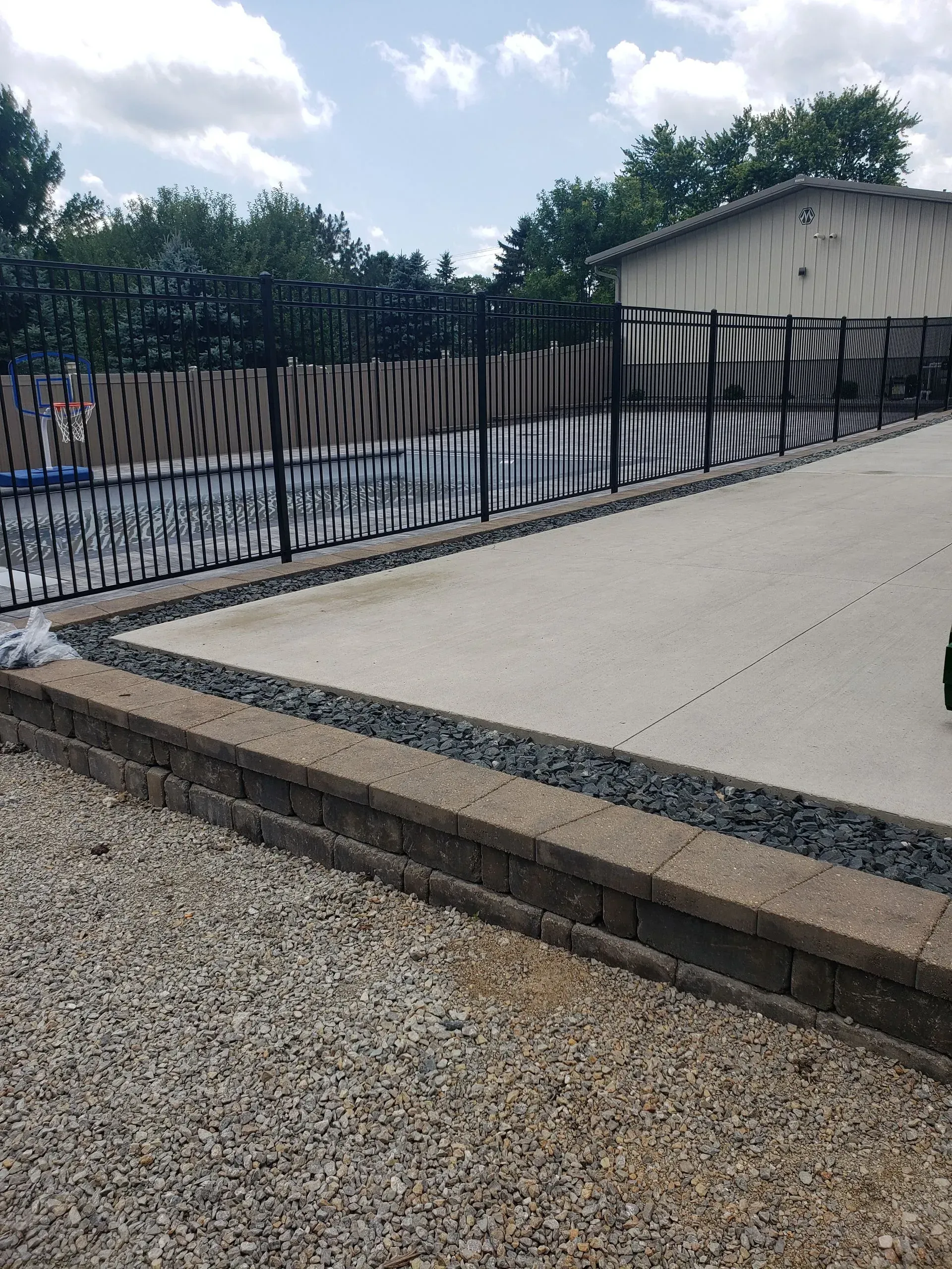 Sloped concrete driveway beside a black metal fence and small white building with graffiti.