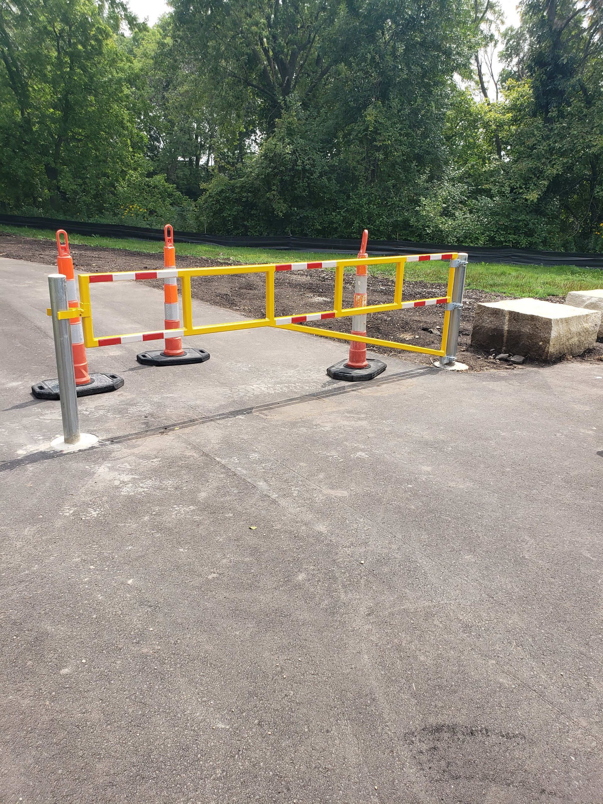 Orange traffic barriers blocking a paved path beside a grassy area and concrete curb.