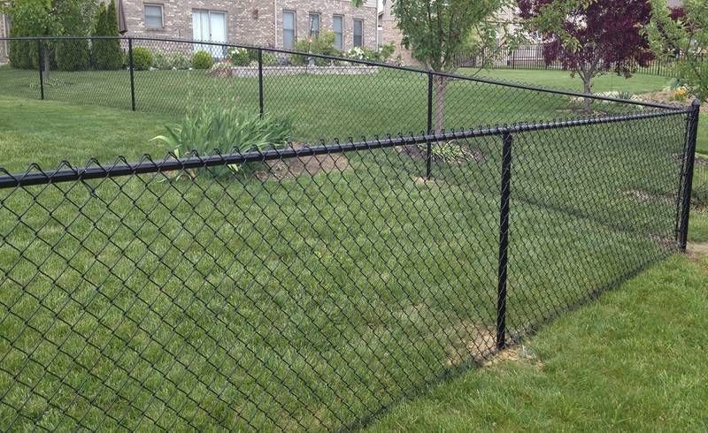 Black chain-link fence enclosing a grassy yard beside a stone building.