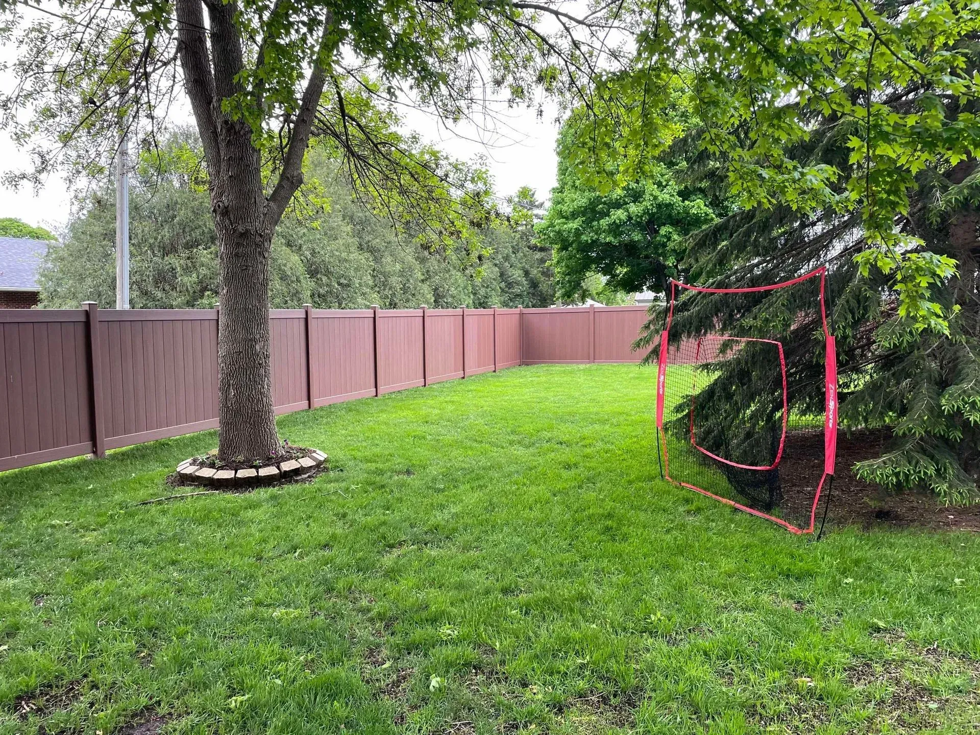 Grassy backyard with pink fence, large trees, and a red netted garden structure on the right