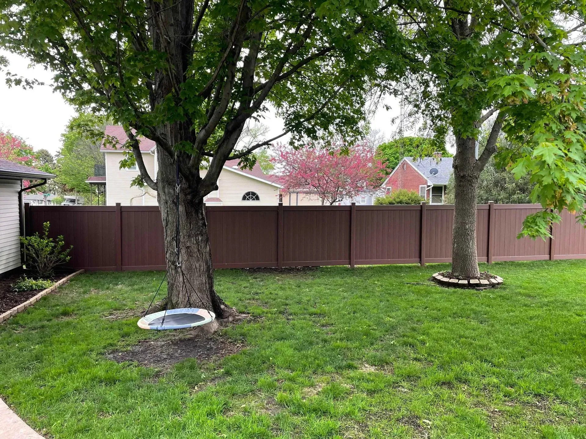 Backyard with two large trees, green lawn, and a brown privacy fence