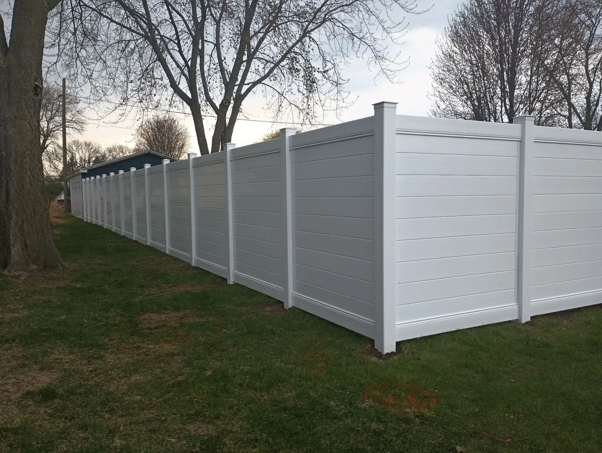White vinyl privacy fence running along a grassy yard with trees in the background.