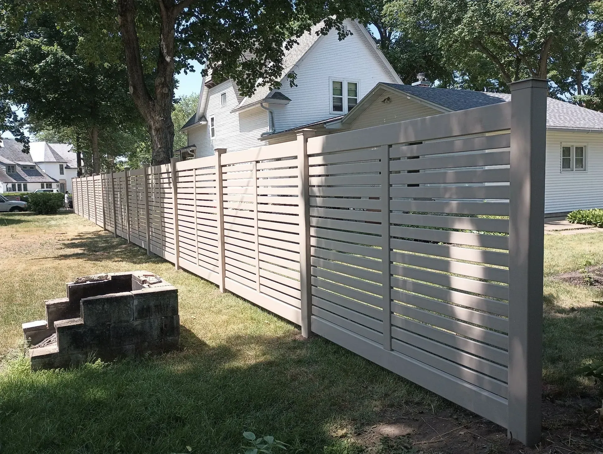 White wooden privacy fence along a grassy yard beside a house in daylight.