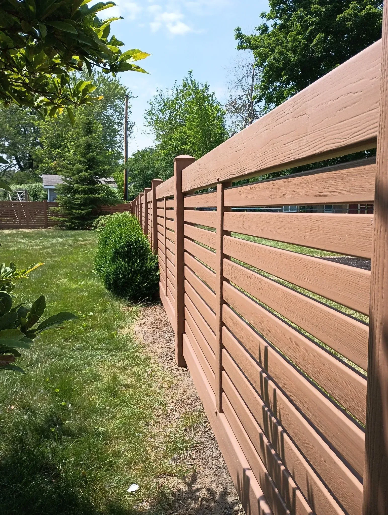 Brown wooden privacy fence along a sunny green garden path under trees