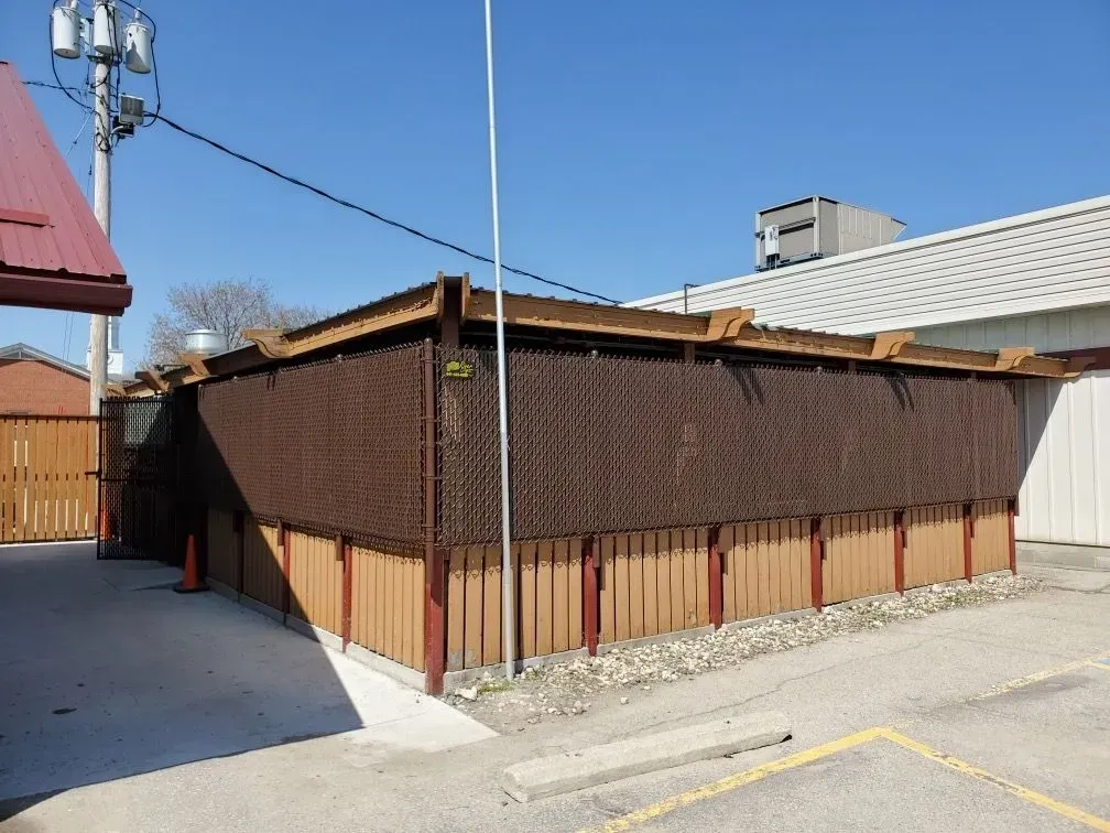 Small brown-sided building with a slanted roof beside a parking lot on a sunny day