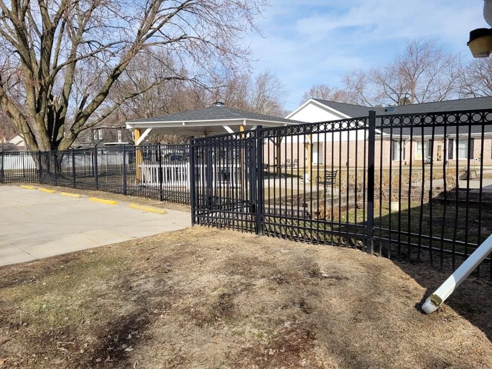 Black metal fence and gate beside a driveway in a suburban yard.
