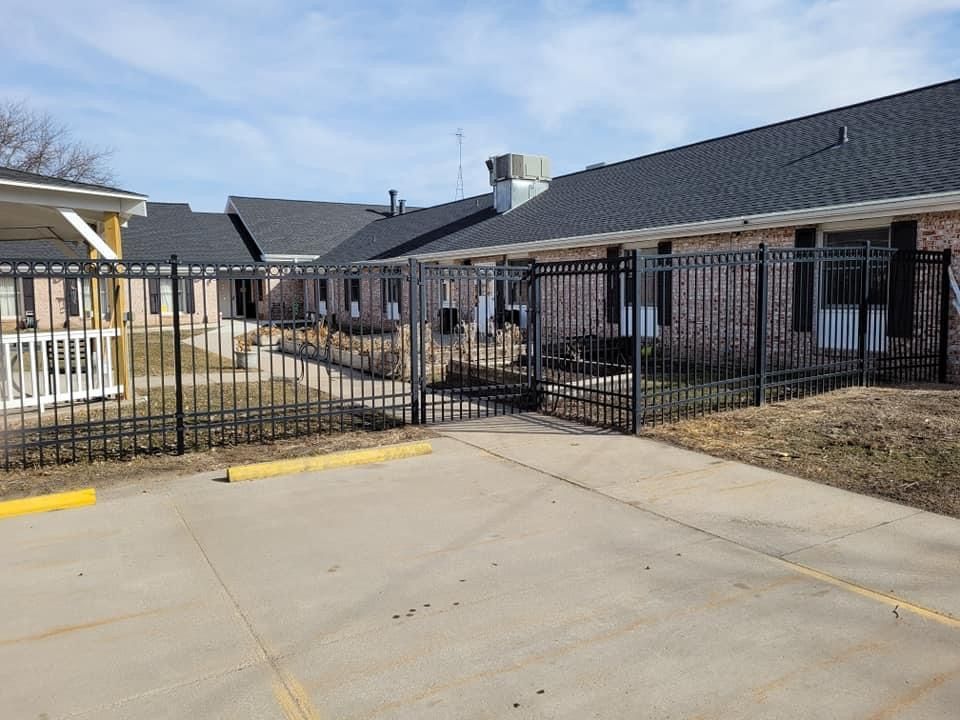 Black metal gate blocking a concrete driveway in front of single-story buildings
