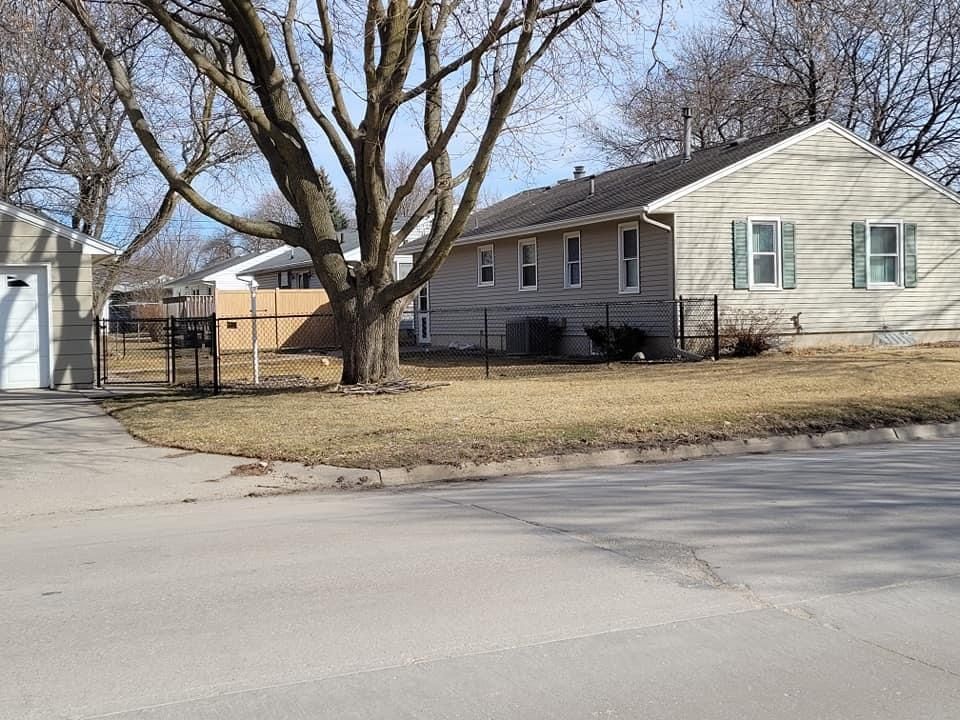 Single-story house with a large tree and a fenced yard along a quiet residential street.