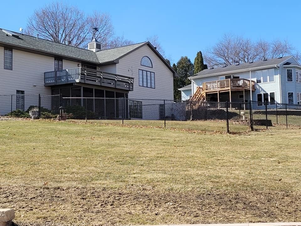 Two houses on a grassy hillside under a clear blue sky, with a covered deck and bare trees.