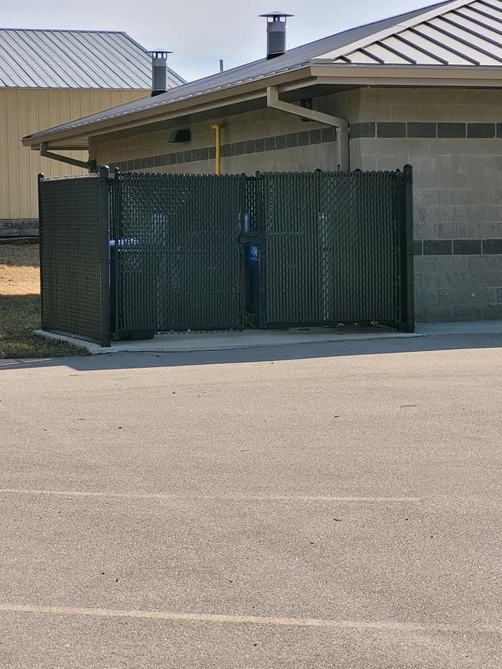Dark green chain-link fence panels blocking a driveway in front of a beige building