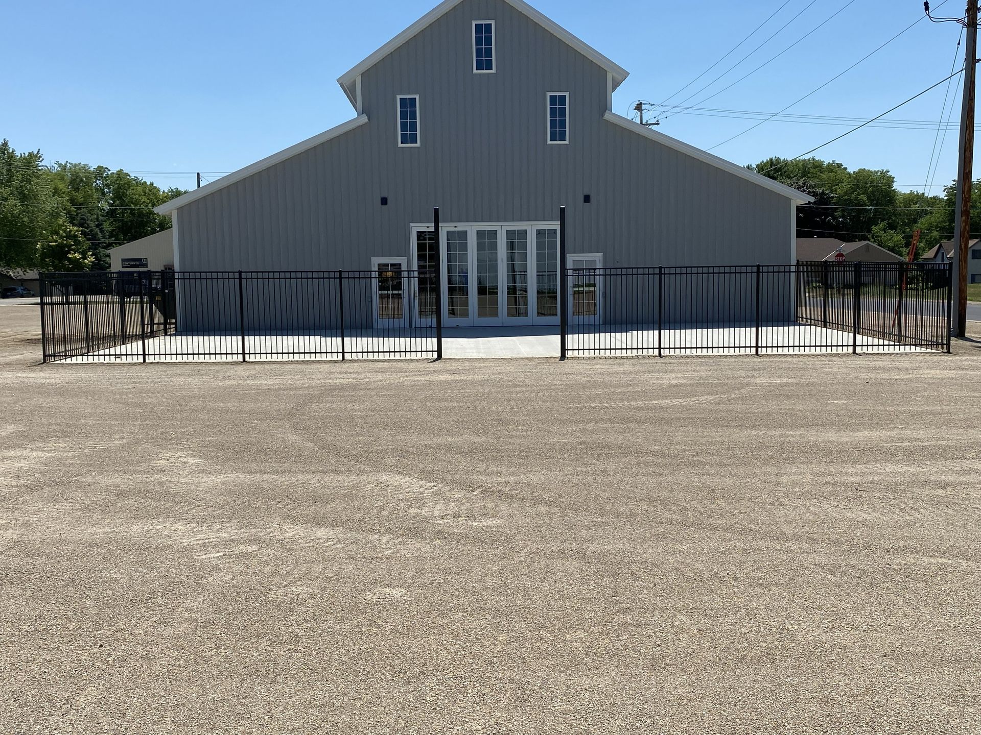 Gray building with a black fence and double glass doors behind a wide paved lot