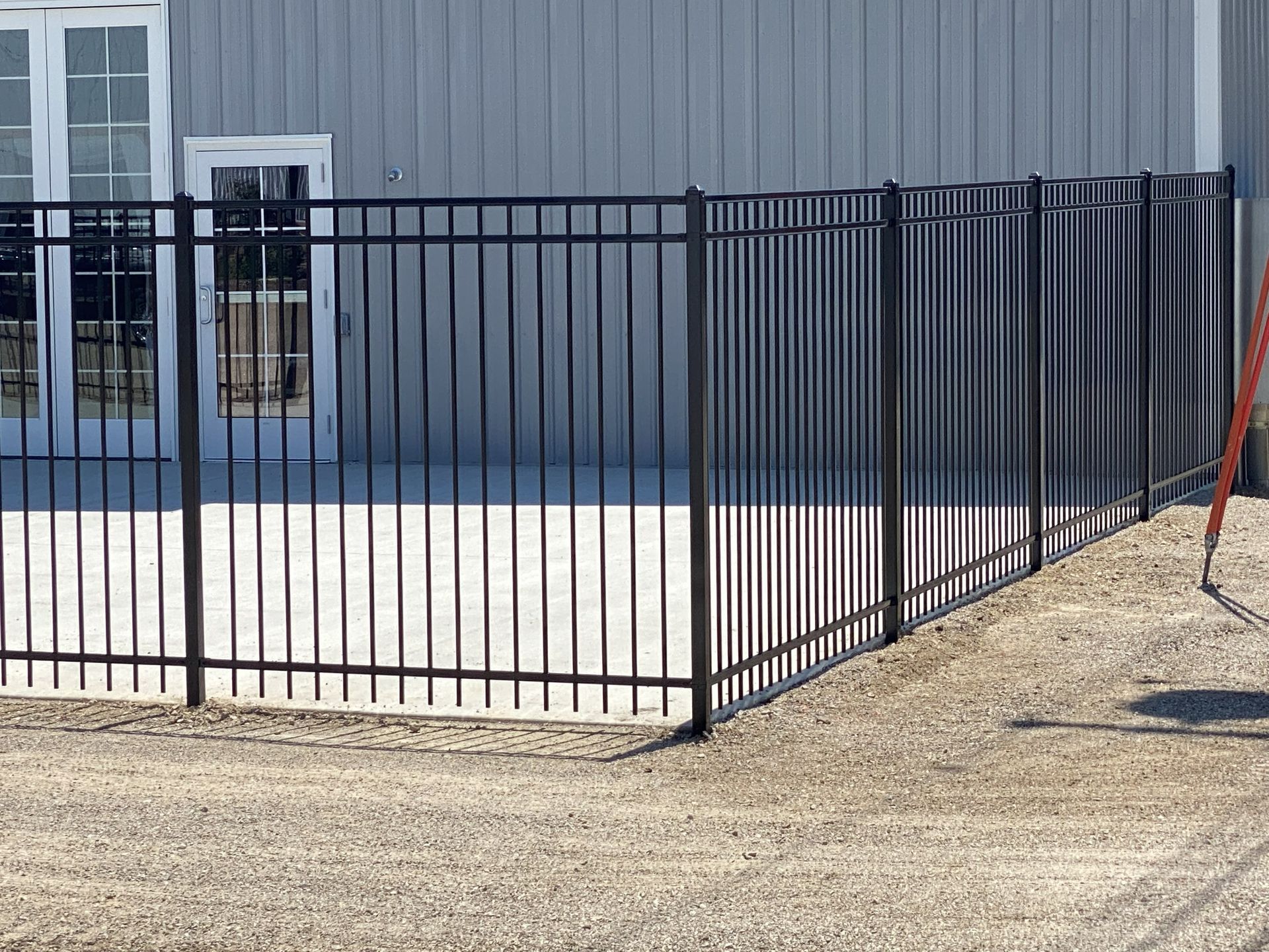 Black metal fence along a gravel lot beside a gray industrial building
