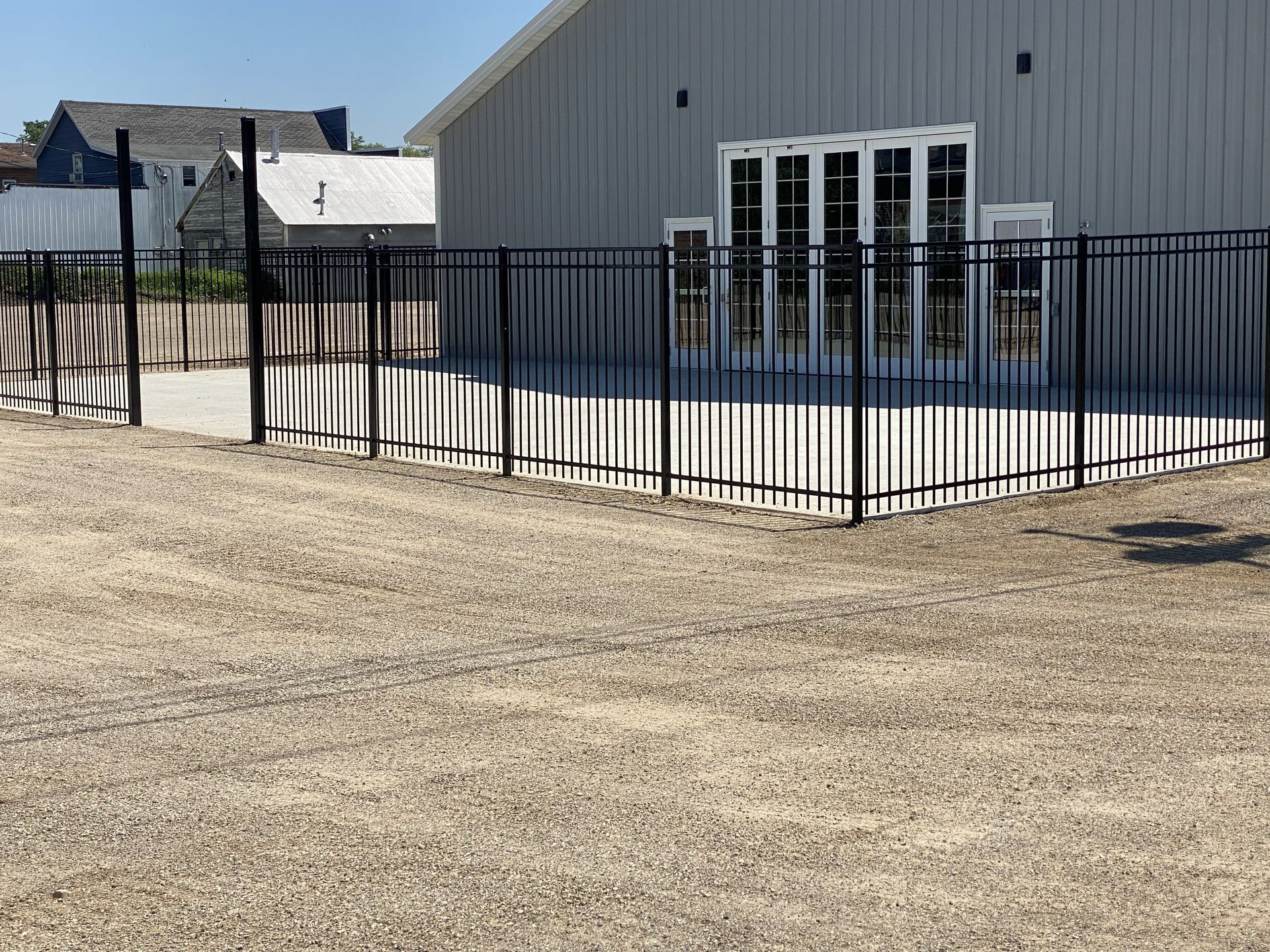 Black metal fence around a gray building with white doors on a gravel lot