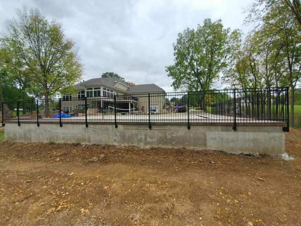 Residential building behind black fence with wet pavement, trees, and muddy foreground