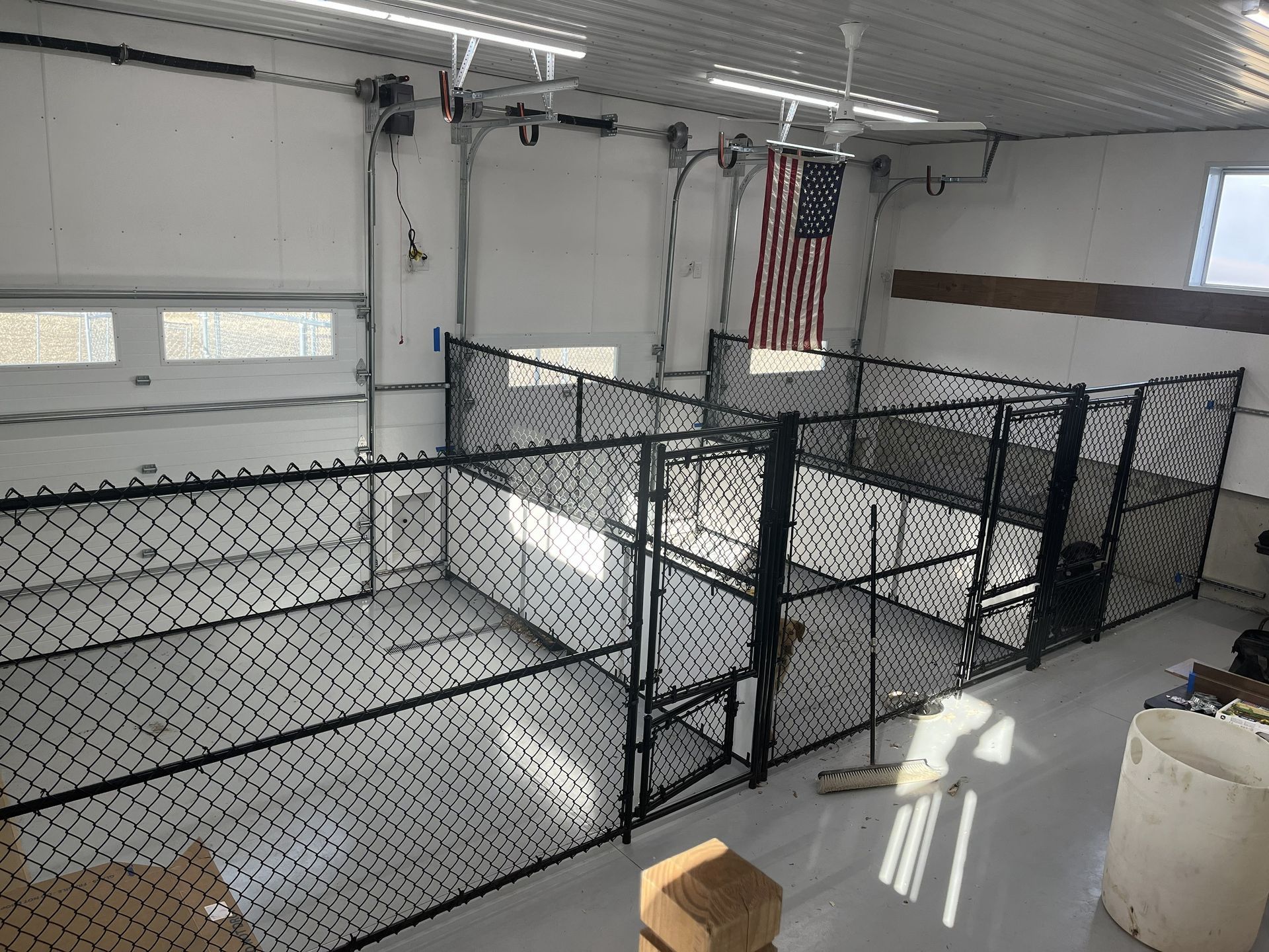 Indoor chain-link fenced kennel area in a bright room with an American flag hanging on the wall.