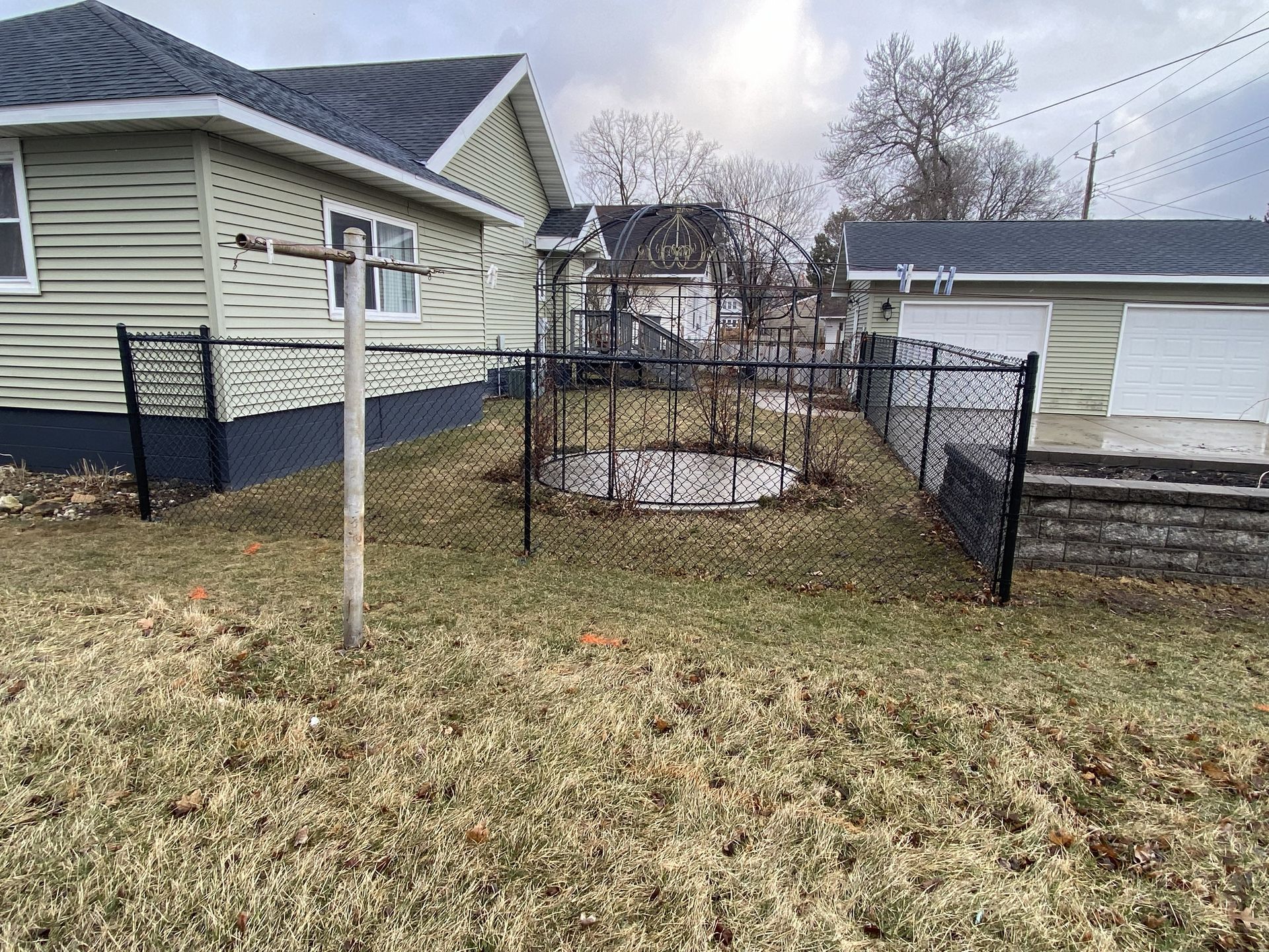 Backyard with a black chain-link fence, leaf-covered grass, and a house and garage in the background