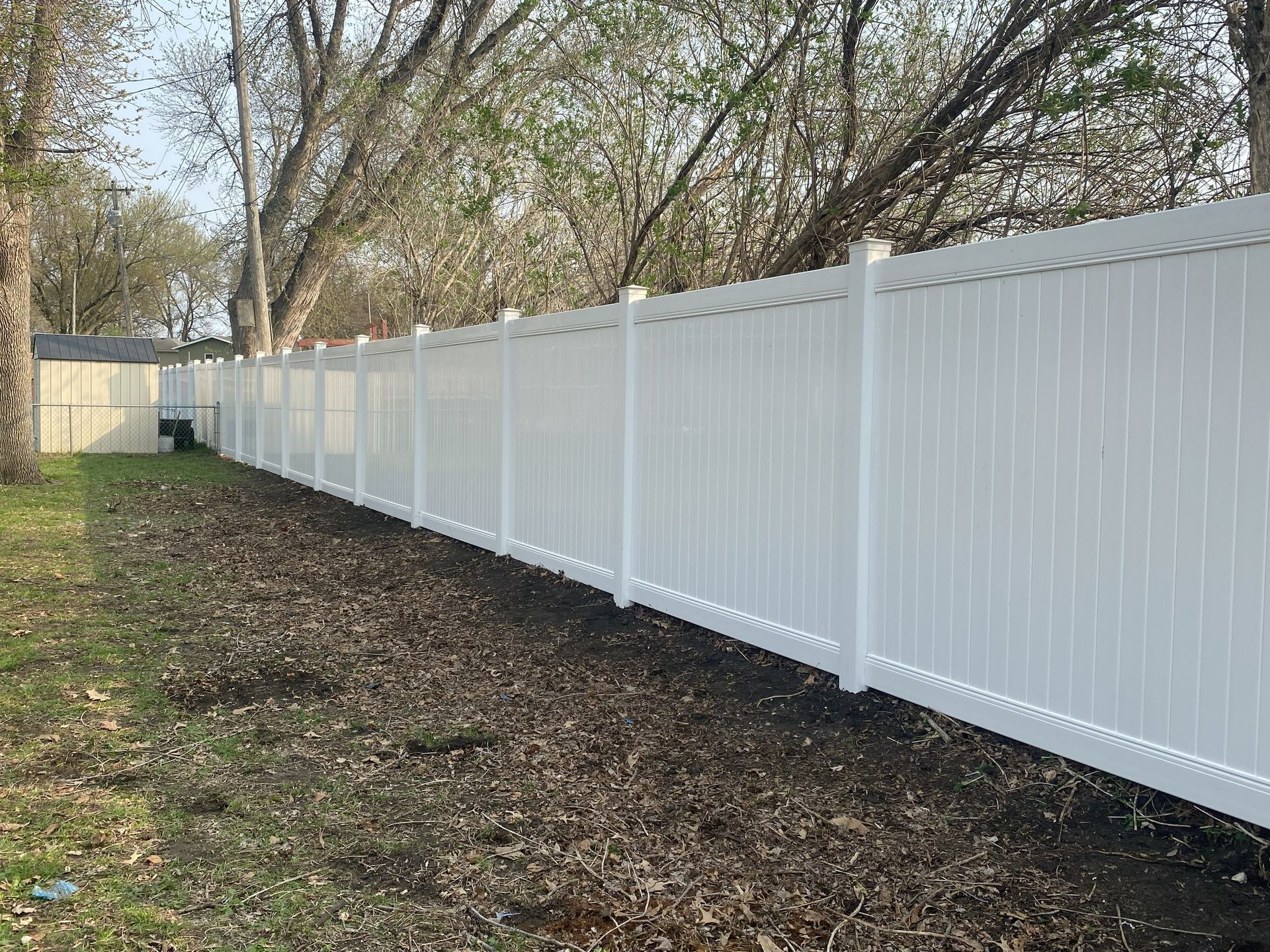 Long white vinyl fence lining a grassy yard with trees overhead
