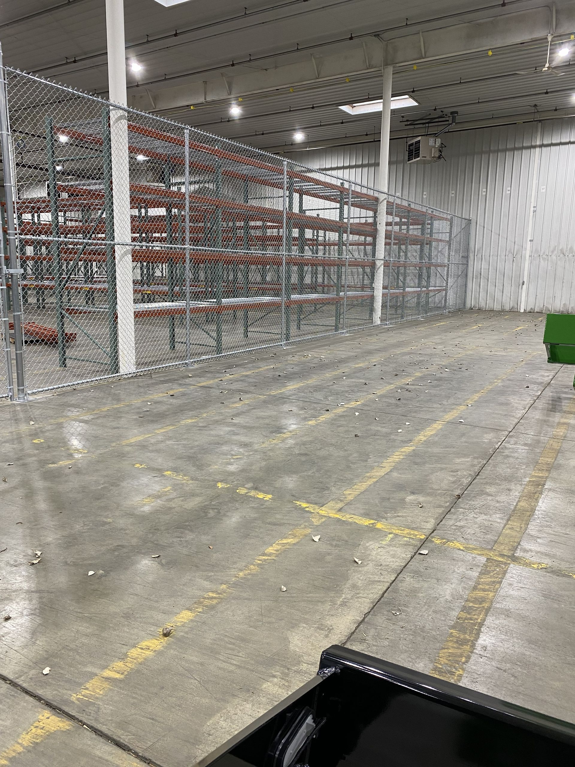 Empty warehouse aisle with concrete floor, tall metal shelving, and overhead lights