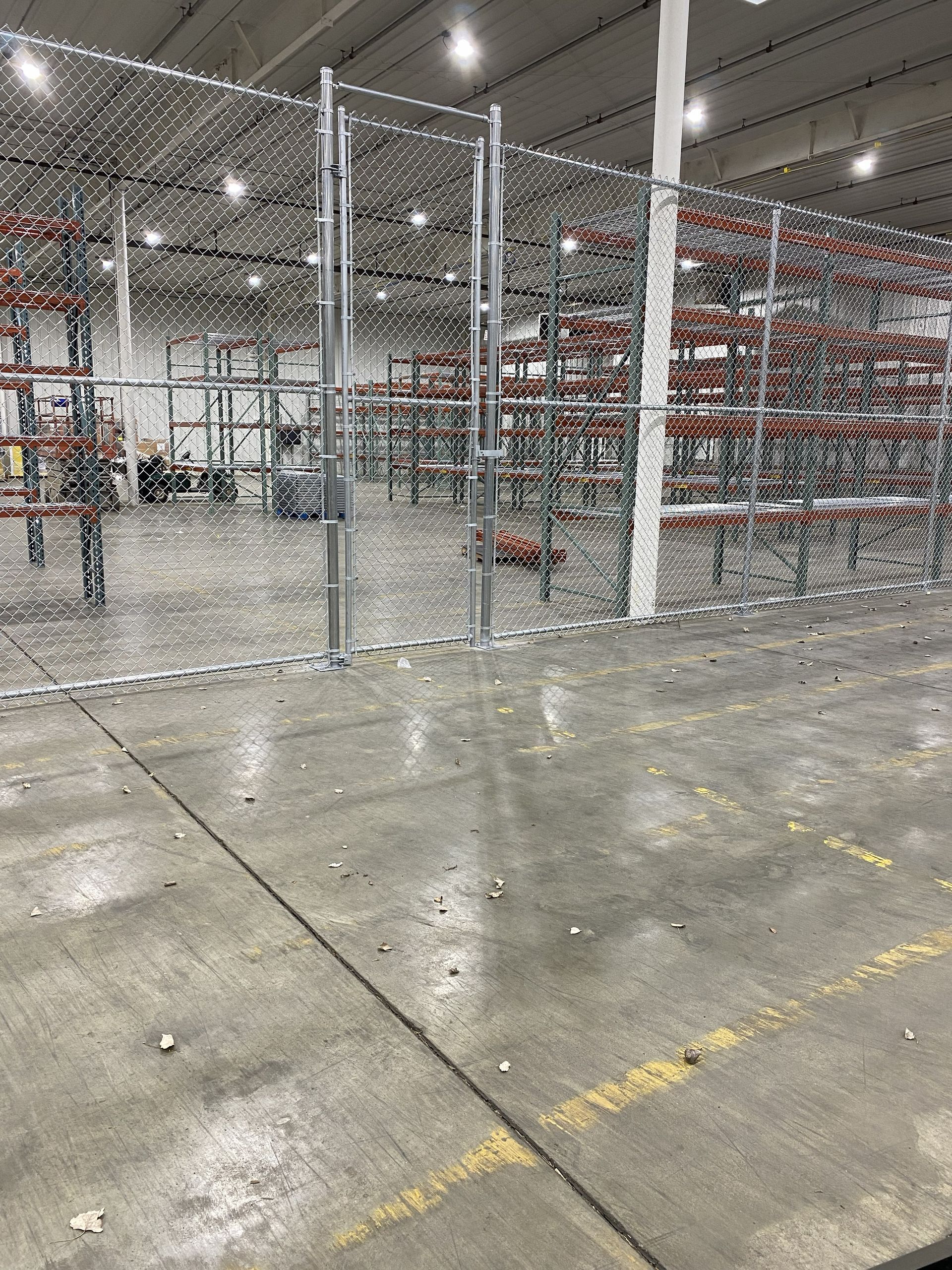Industrial warehouse aisle with wire fencing, metal racks, and polished concrete floor.