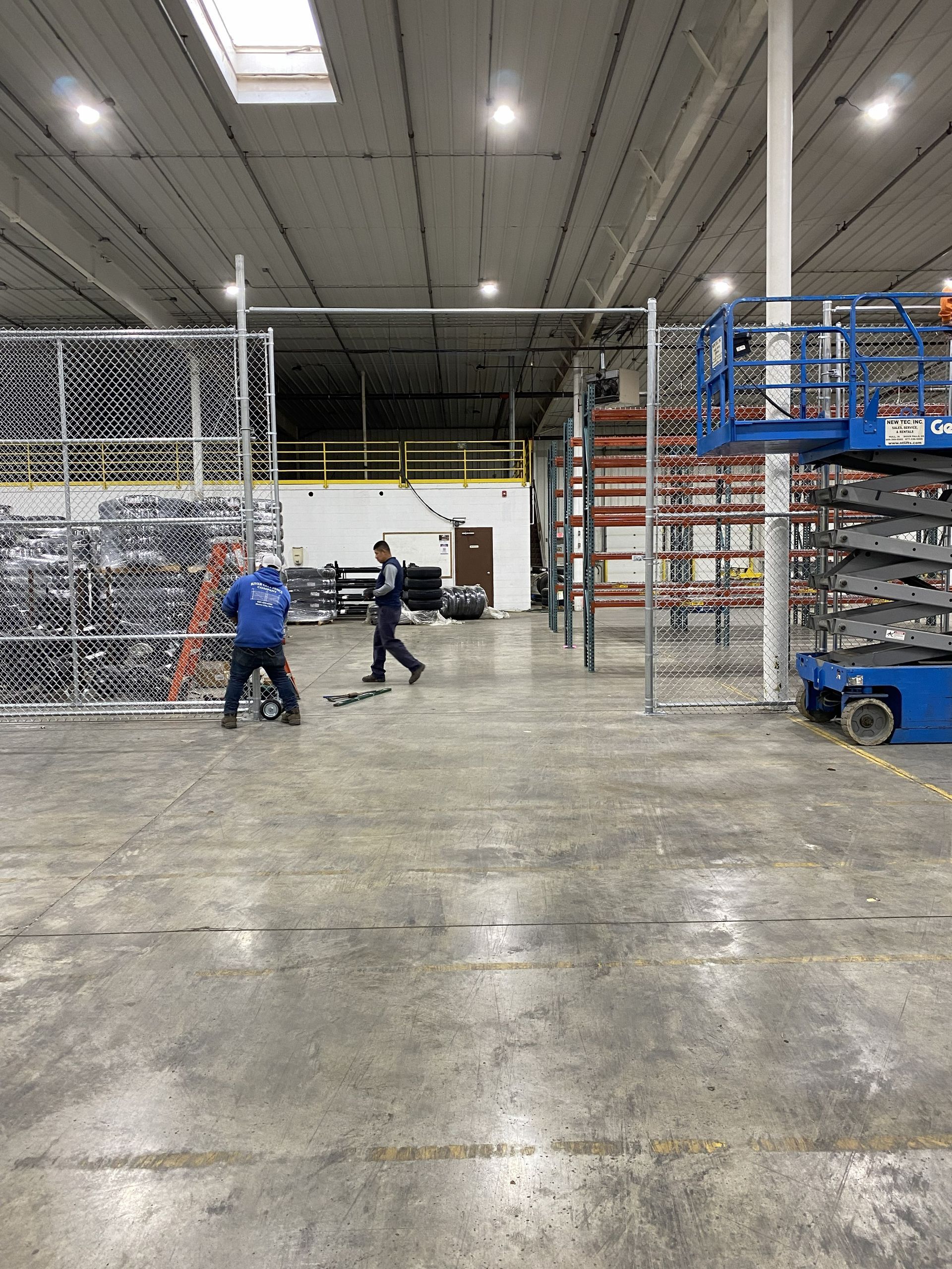 Warehouse interior with two workers near shelving and a blue cart on a concrete floor