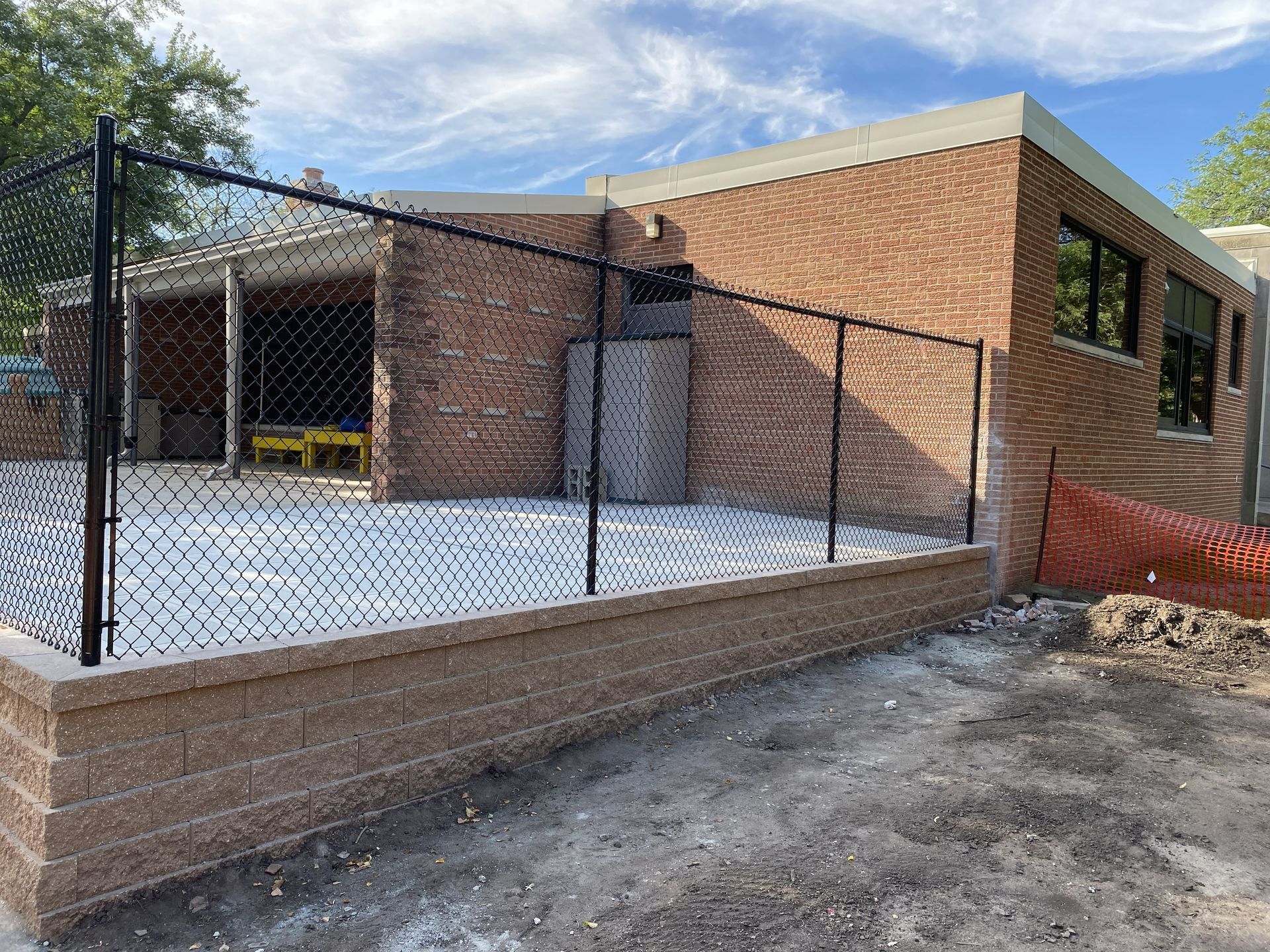 Brick building with chain-link fence and gated concrete lot under a blue sky