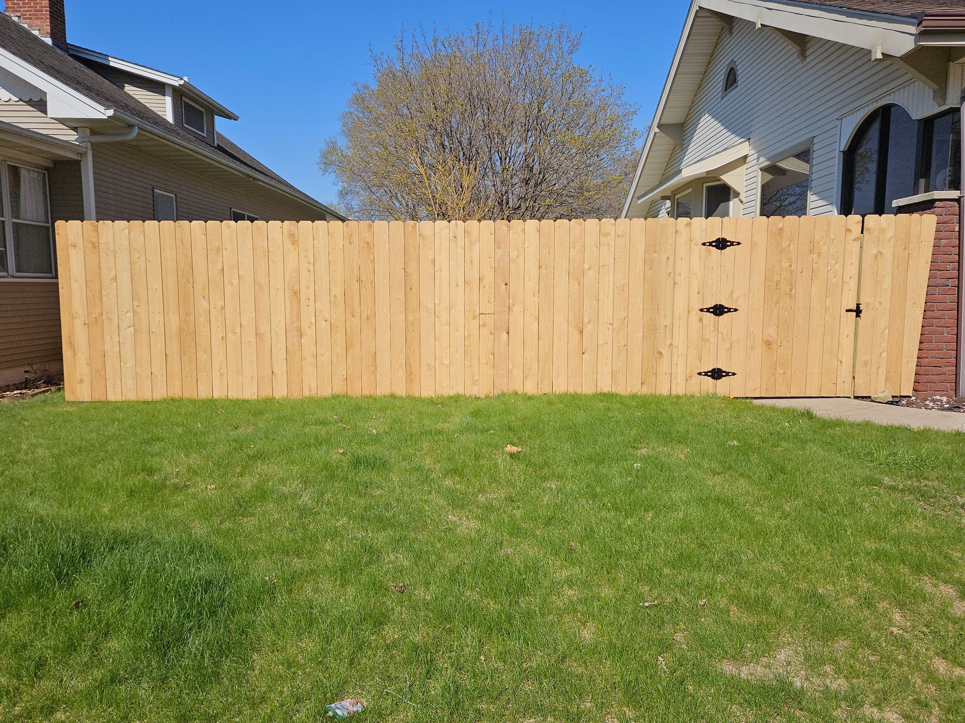 Wooden privacy fence across a grassy backyard between two houses under a clear sky