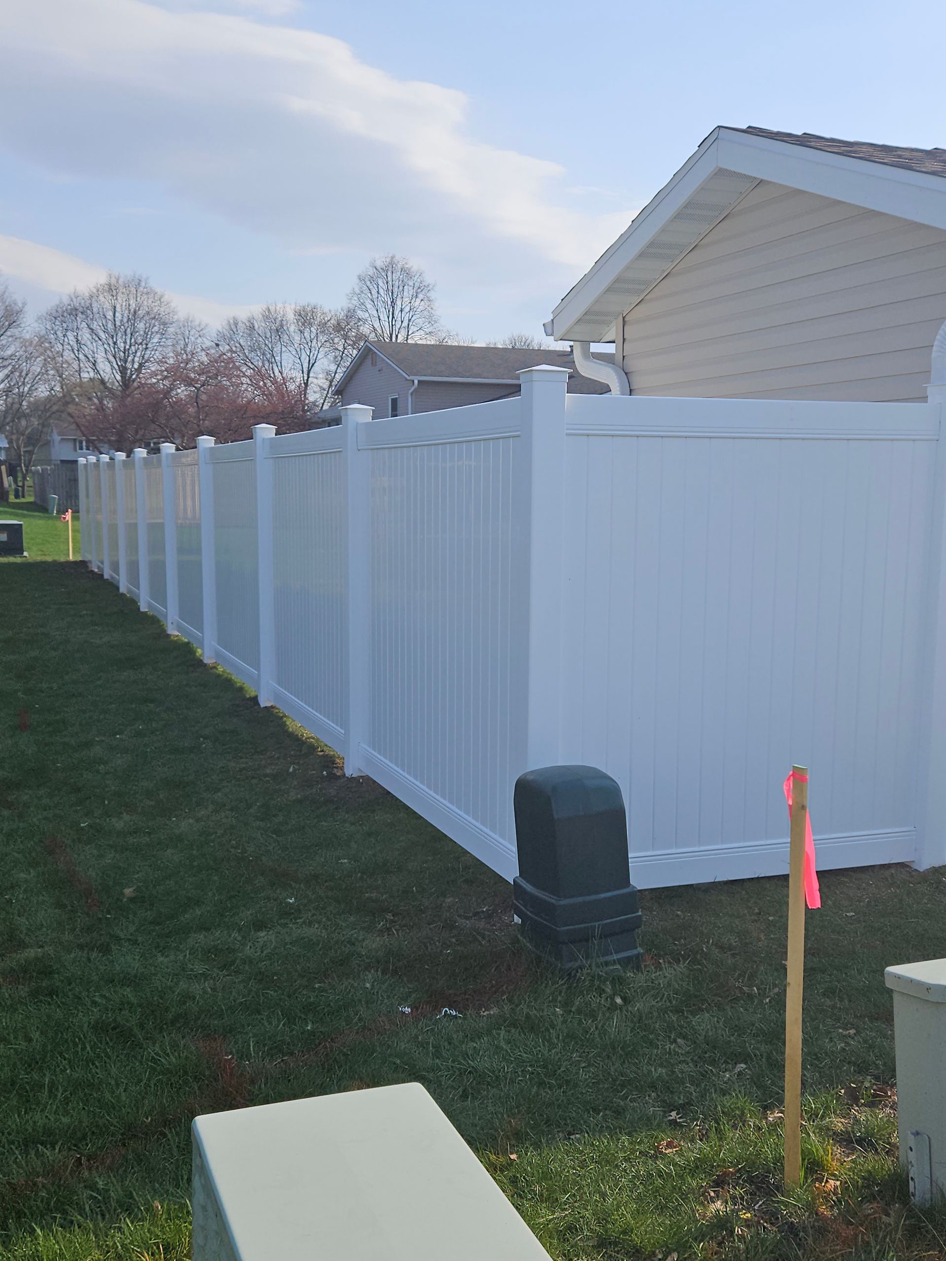 White vinyl privacy fence along a grassy backyard beside a house, with a utility box in the foreground.