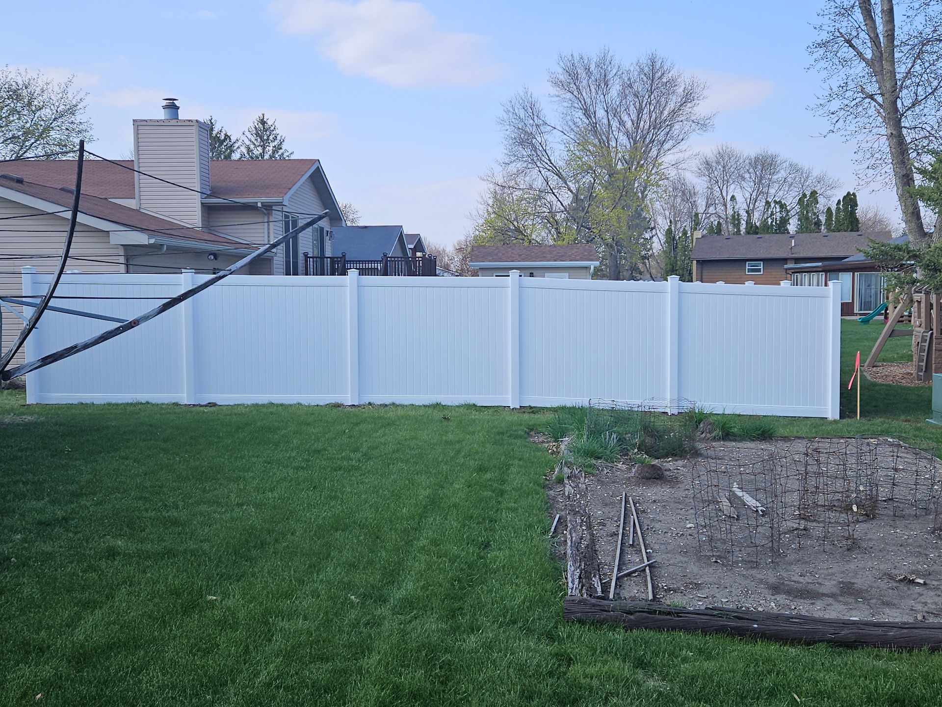 Backyard with white vinyl fence, green lawn, and garden beds at dusk