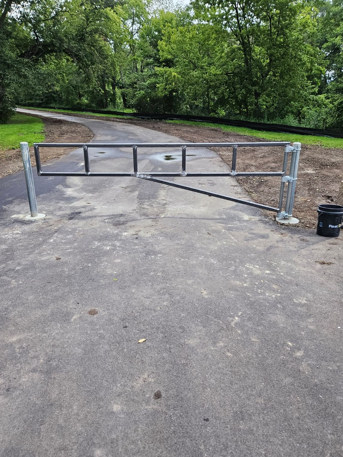 Metal gate across a paved park path beside trees and gravel trail