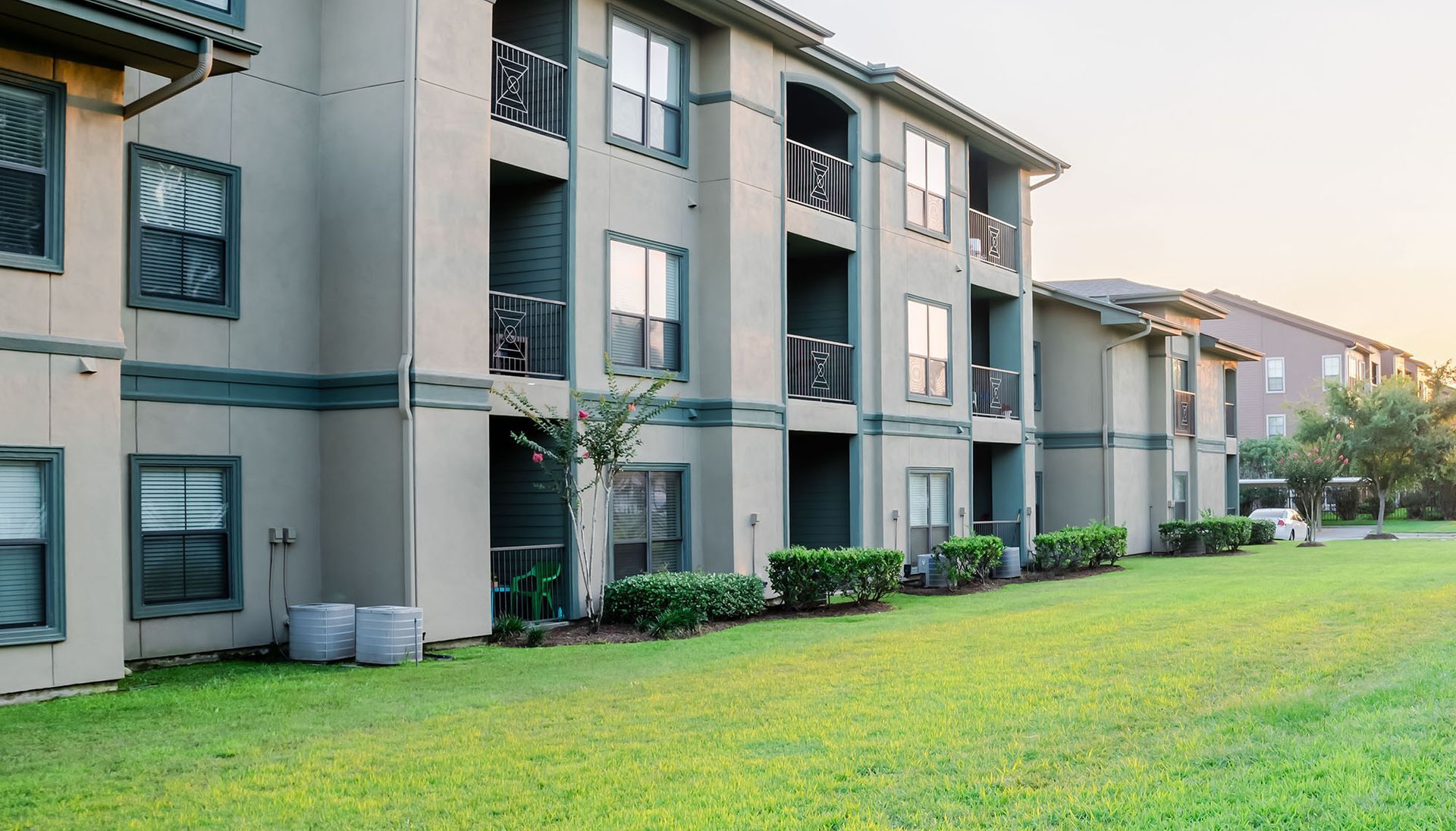 Apartment building with beige exterior, balconies, and green lawn; daytime.