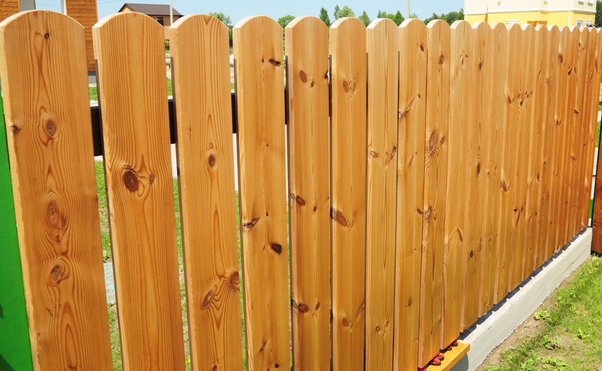 Wooden privacy fence with vertical slats and rounded tops along a green yard