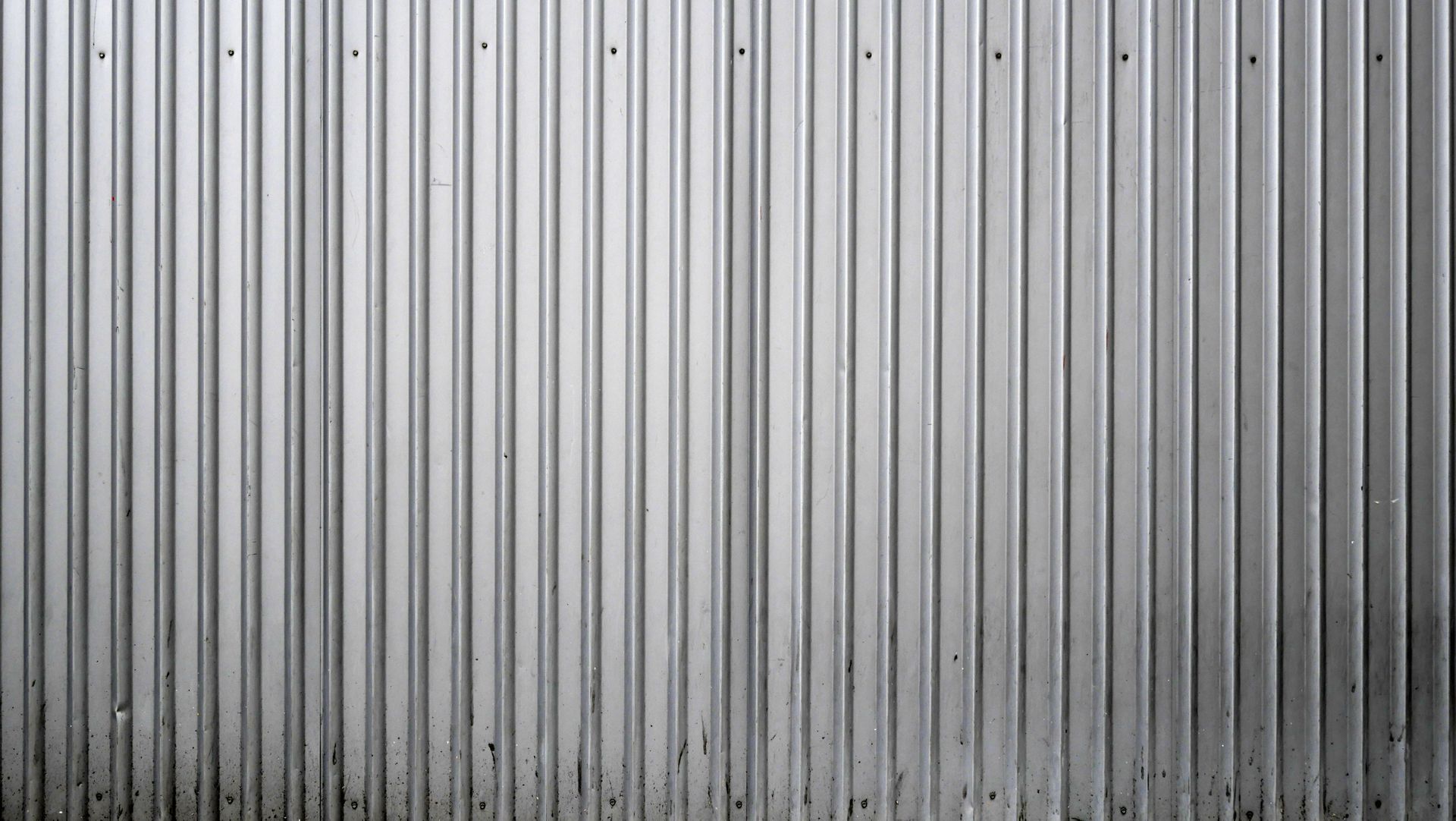 Gray corrugated metal wall with vertical ridges and dark stains near the bottom
