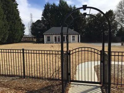 Black iron gate and fence opening to a dry yard with a small house and trees behind it