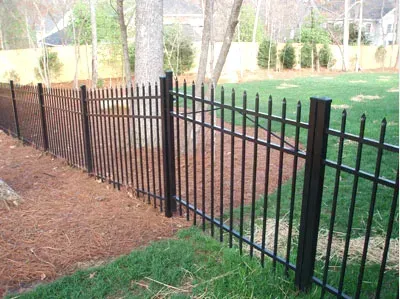 Black metal fence along a mulched and grassy backyard edge with trees in the background