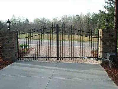 Closed black wrought-iron gate across a concrete driveway between brick pillars
