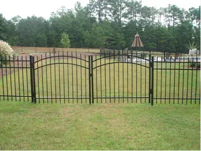 Black metal fence across a grassy yard with trees and a patio umbrella in the background