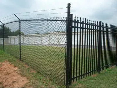 Black metal fence and gate beside a chain-link fence around a grassy field under a cloudy sky