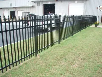 Black metal fence along a grassy yard beside a white building and paved area.