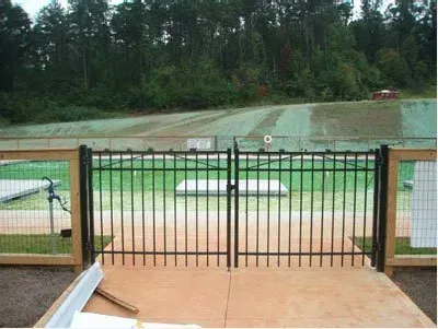 Metal gate overlooking a grassy sports field with trees in the background