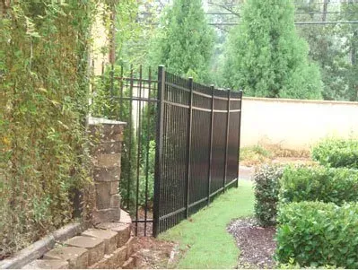 Black metal fence along a garden path beside hedges and a stone wall