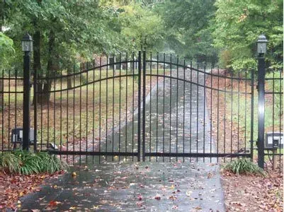 Black wrought-iron gate blocking a wet driveway lined with trees and autumn leaves