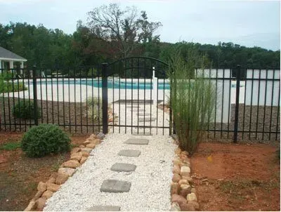 Backyard pool behind black metal fence, with a white gravel path and stone stepping stones.